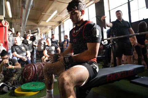 A lifter chalks his hands on the bench while the crowd waits behind him.
